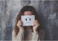 Дівчина тримає папір із сумним смайлом, закриваючи обличчя - PSYCHOLOGUS